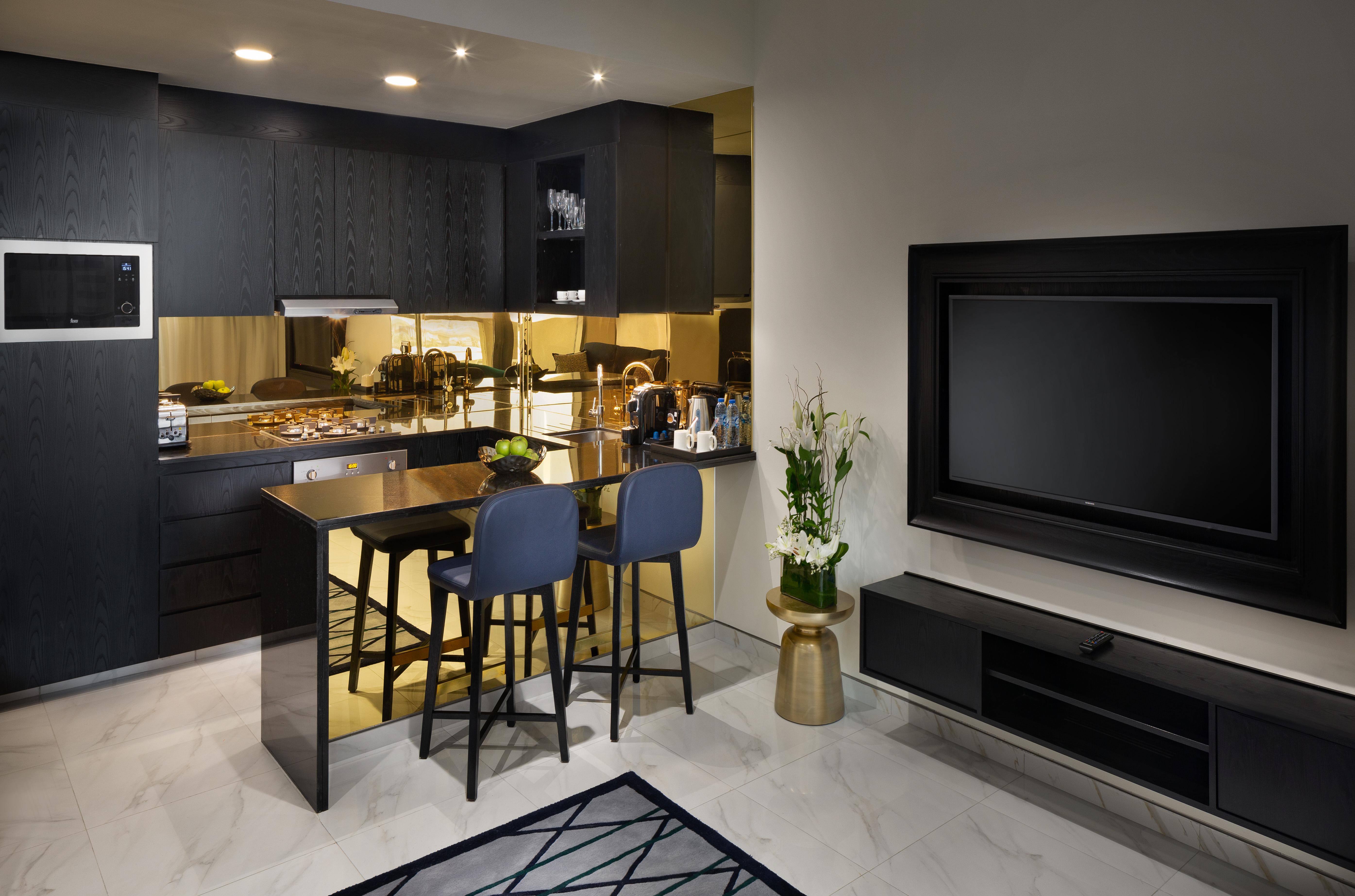 Aparthotel Millennium Atria Business Bay Dubaj Exteriér fotografie The photo depicts a modern kitchen and living area. The kitchen features dark cabinetry with a clean design, showcasing various appliances, including a stovetop and possibly an oven. There is a kitchen island with two stools, suggesting a space for c
