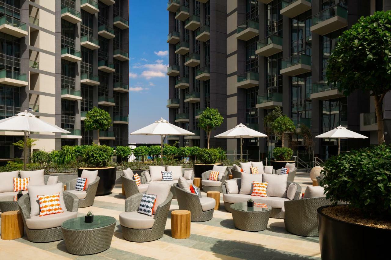 Aparthotel Millennium Atria Business Bay Dubaj Exteriér fotografie The photo shows a modern outdoor lounge area, featuring several comfortable seating arrangements made of soft, stylish lounge chairs and round tables. The seating is adorned with colorful pillows, adding a pop of color to the neutral tones of the fur